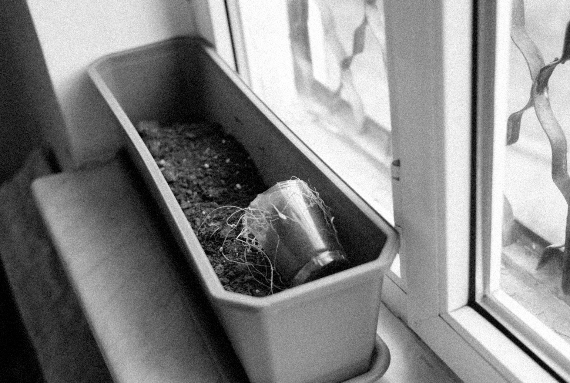 Close-up of an empty planter on a windowsill with soil and a glass jar.
