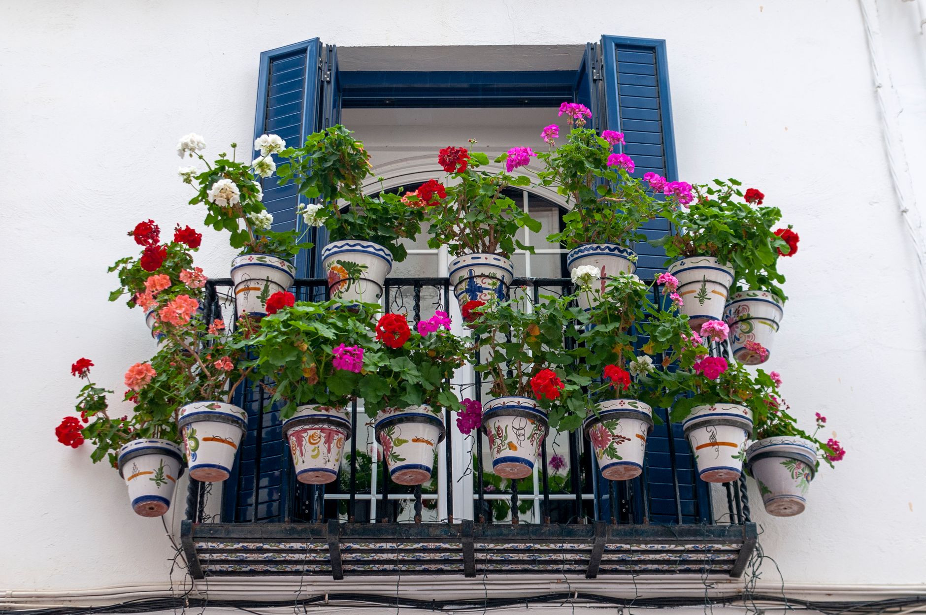 Vibrant geraniums adorn a balcony in Sitges, Spain, creating a bright and lively facade.